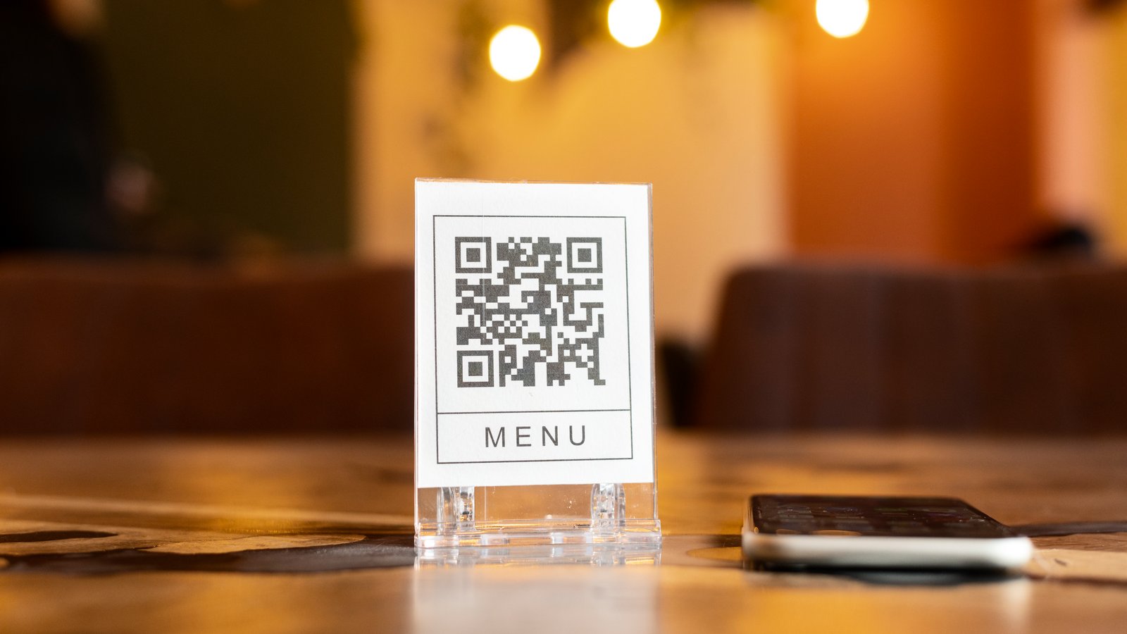 QR-kódos étlap tábla egy étterem asztalán, mellette egy telefon